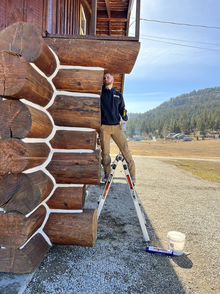 Eli performing exterior log home restoration on a ladder
